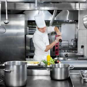 Chef in hotel or restaurant kitchen cooking, he is seasoning dishes.